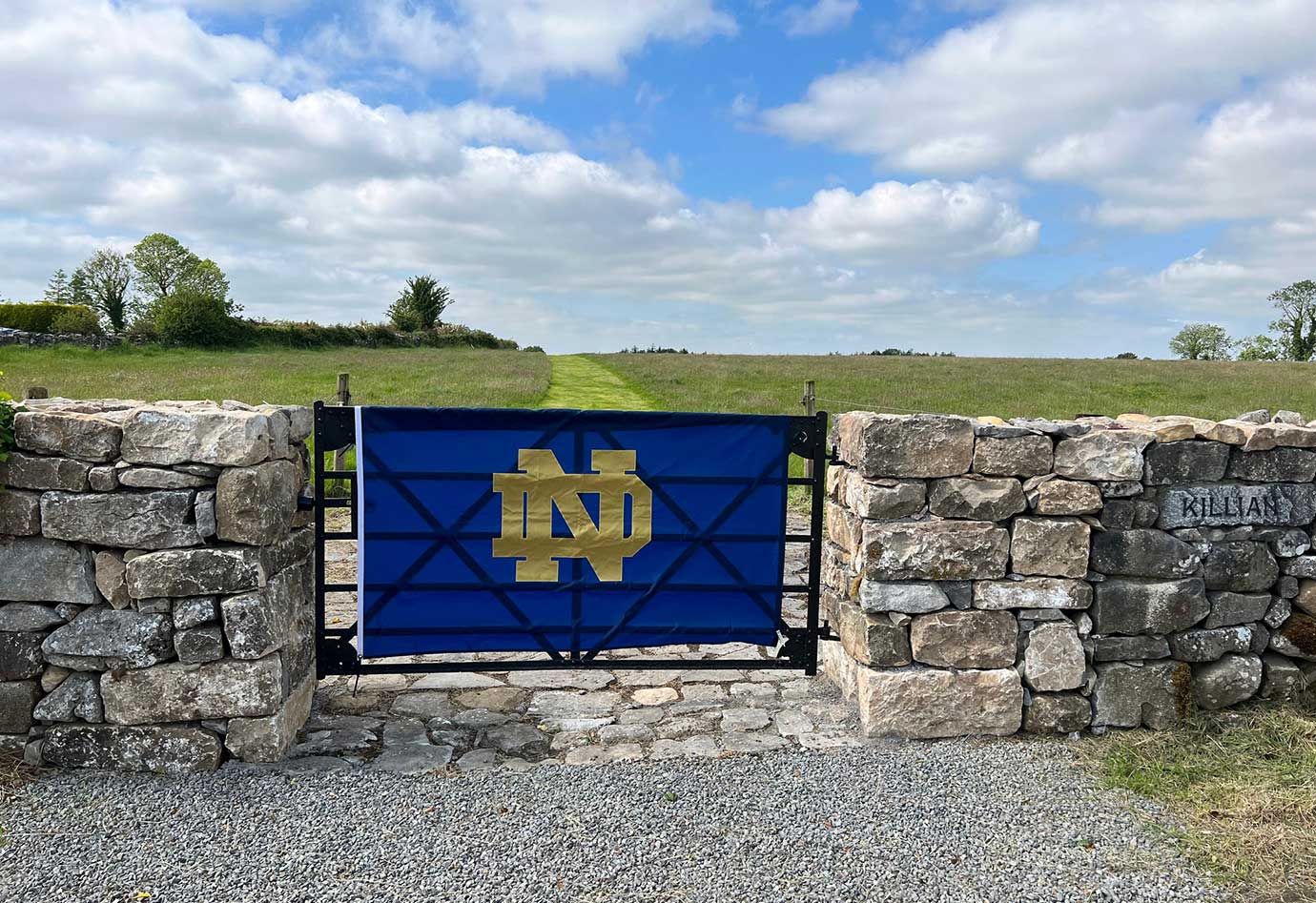 Notre Dame Flag hung on a gate by a field.